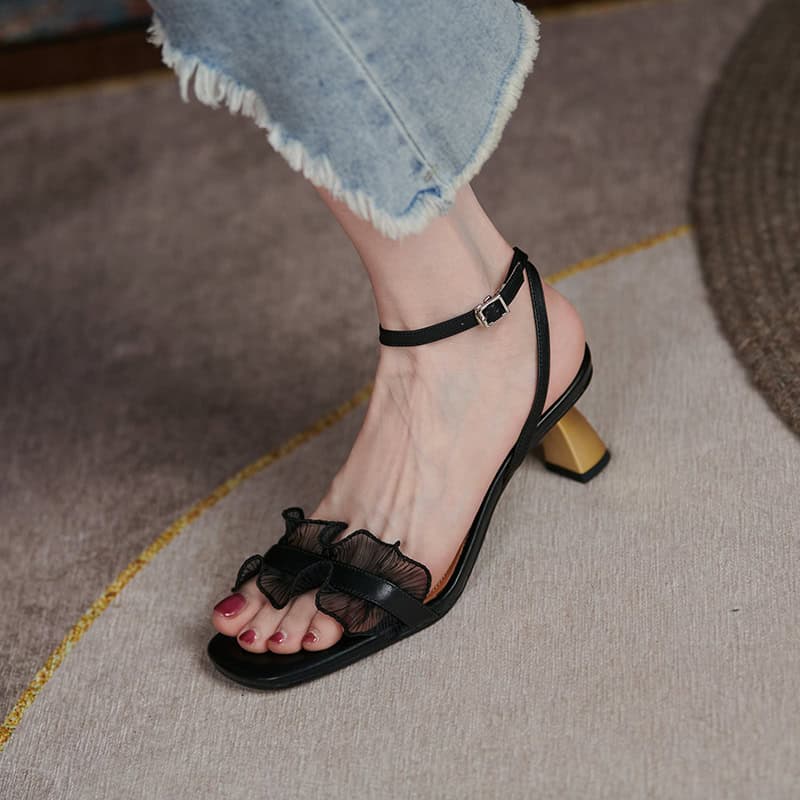Elegant black high heel sandal with ruffle detail, ankle strap, and stylish square heel for women. Perfect for fashion-forward footwear and elegant occasions.