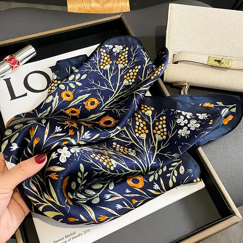 Luxurious navy silk scarf with floral print featuring white, orange, and green accents, perfect for stylish accessories and optical eye-catching fashion statements.