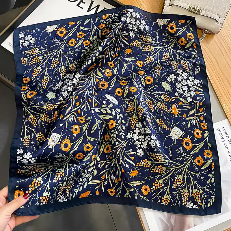 Vibrant navy silk scarf with intricate orange, white, and green floral patterns, perfect for fashionable accessory and versatile styling.