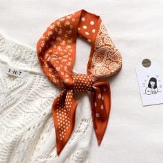 Elegant orange bandana with white paisley and polka dot patterns, perfect for fashion accessories.