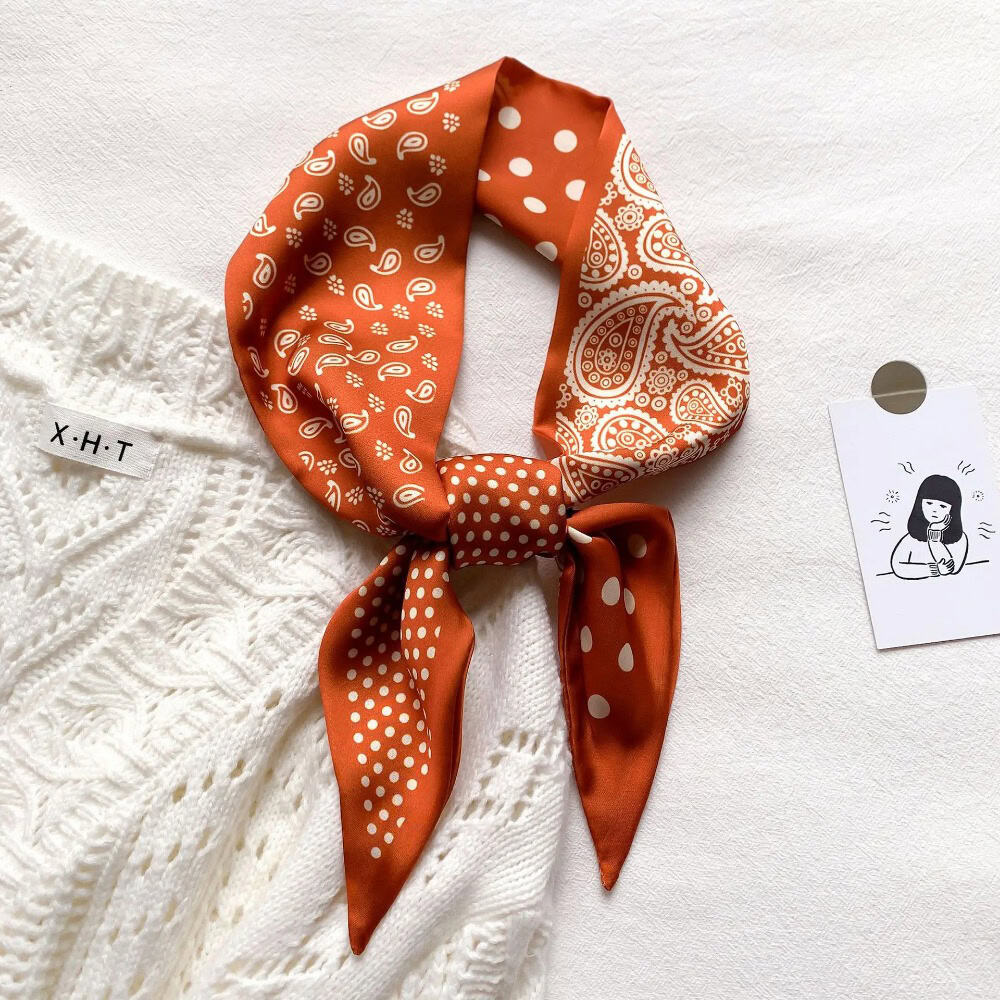 Elegant orange bandana with white paisley and polka dot patterns, perfect for fashion accessories.