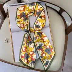 Bright, floral patterned silk scarf with a yellow, white, red, and navy blue color scheme, featuring a green border, perfect for elegant styling.