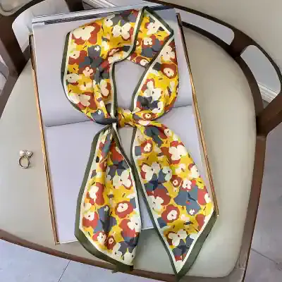 Bright, floral patterned silk scarf with a yellow, white, red, and navy blue color scheme, featuring a green border, perfect for elegant styling.