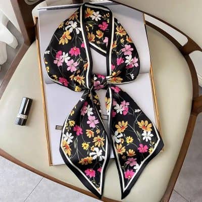 Elegant floral patterned silk scarf with vibrant pink, white, and yellow flowers on a black background, perfect for fashion accessories and stylish embellishments.