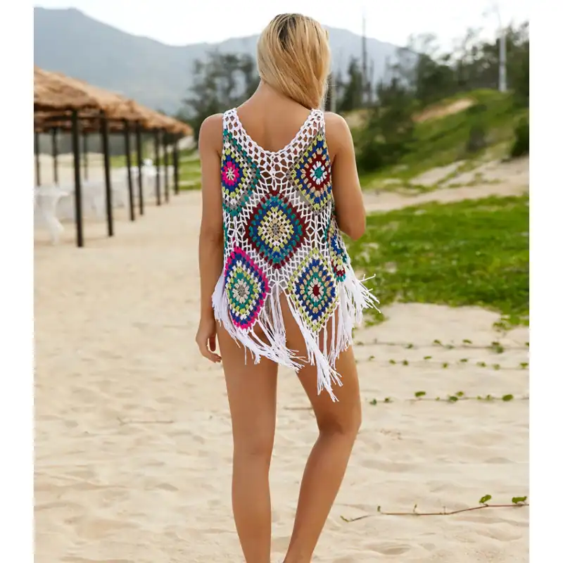 A woman wearing a colorful crochet beach cover-up on the sand with scenic mountains and greenery in the background. Perfect for summer beachwear and vacation styles.