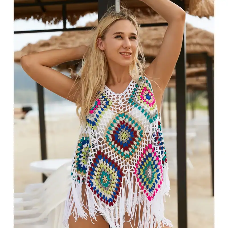 A young woman wearing a colorful crochet beach coverup with intricate patterns, standing outdoors near a beach hut, enjoying sunny weather and ocean views, perfect for summer beachwear.
