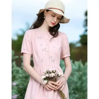 Beautiful young woman in a pink embroidered dress with a sun hat holding a bouquet of flowers, perfect for stylish summer outings and fashion accessories.