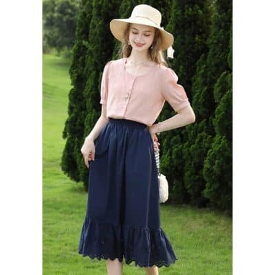 Elegant pink blouse and navy long skirt worn by a woman in a garden setting, showcasing fashionable summer clothing and accessories for women.