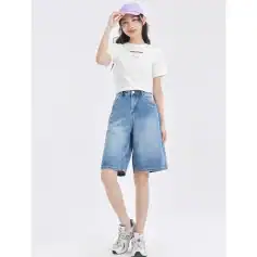 Young woman in casual denim bermuda shorts and white t-shirt, wearing a pastel purple cap, standing confidently with a minimalistic background, embodying trendy and comfortable fashion from Monalisa Medical's store.