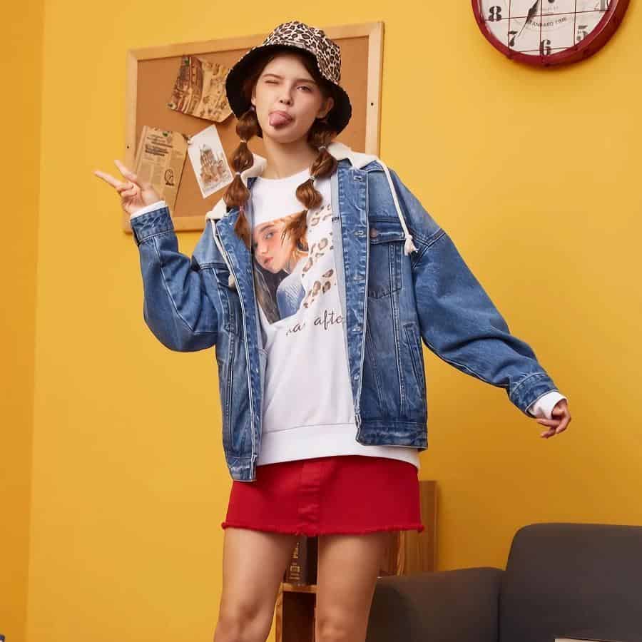 Brightly colored casual outfit for kids, featuring a denim jacket, printed hoodie, red skirt, and playful accessories in a lively indoor setting.