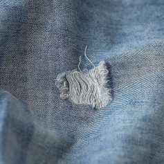 Close-up of a ripped denim fabric with visible threads, highlighting denim repair or distressed fashion style for opt modernization and casual wear.