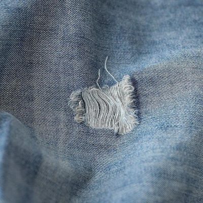 Close-up of a ripped denim fabric with visible threads, highlighting denim repair or distressed fashion style for opt modernization and casual wear.