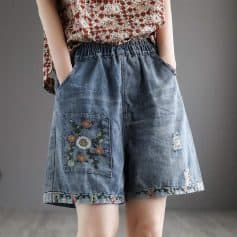 Embroidered denim shorts with floral patchwork and distressed details, perfect for stylish casual wear. Features an elastic waistband and deep pockets for comfort.