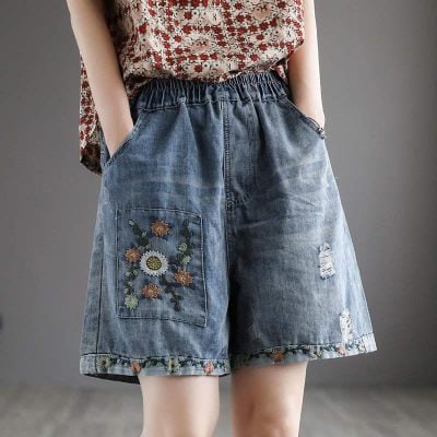 Embroidered denim shorts with floral patchwork and distressed details, perfect for stylish casual wear. Features an elastic waistband and deep pockets for comfort.