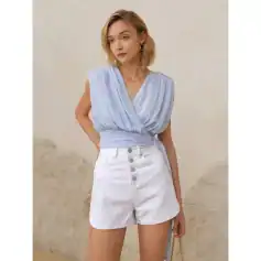 Fashionable light blue sleeveless wrap top paired with high-waisted white denim shorts featuring button-front closure, perfect for trendy summer outfits and casual wear.