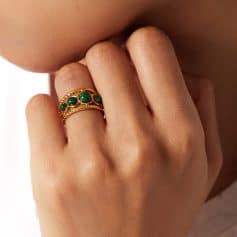 Close-up of a gold ring with green malachite stones worn on a woman's finger, showcasing luxurious jewelry for women seeking stylish accessories.