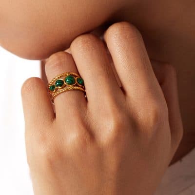 Close-up of a gold ring with green malachite stones worn on a woman's finger, showcasing luxurious jewelry for women seeking stylish accessories.