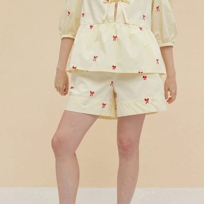 Comfortable women's pajamas set featuring a cream-colored top and shorts adorned with red bow patterns, perfect for relaxed lounging and sleepwear.