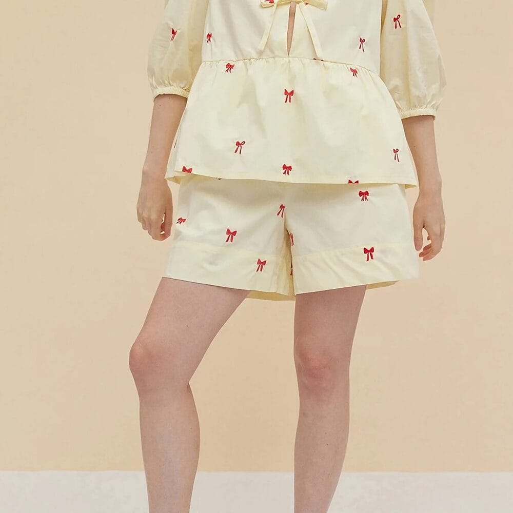 Comfortable women's pajamas set featuring a cream-colored top and shorts adorned with red bow patterns, perfect for relaxed lounging and sleepwear.