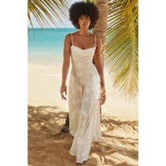 Beautiful woman in a stylish white floral dress on a tropical beach with palm trees and ocean backdrop.