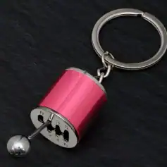 Miniature motorcycle gear shift keychain accessory with metallic pink finish, rubberized grip, and silver ball shifter design. Perfect for motorcycle enthusiasts and as a trendy keyring.