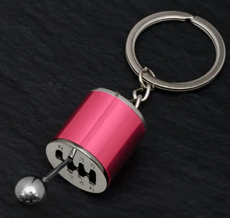 Miniature motorcycle gear shift keychain accessory with metallic pink finish, rubberized grip, and silver ball shifter design. Perfect for motorcycle enthusiasts and as a trendy keyring.