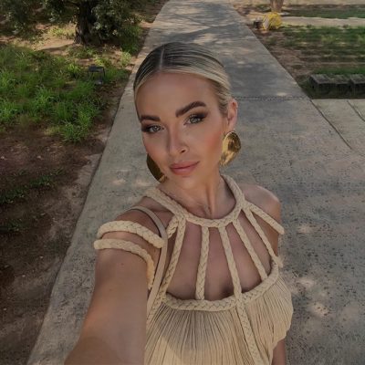 Woman wearing fashionable dress with bold jewelry, walking outdoors on a sunny day.