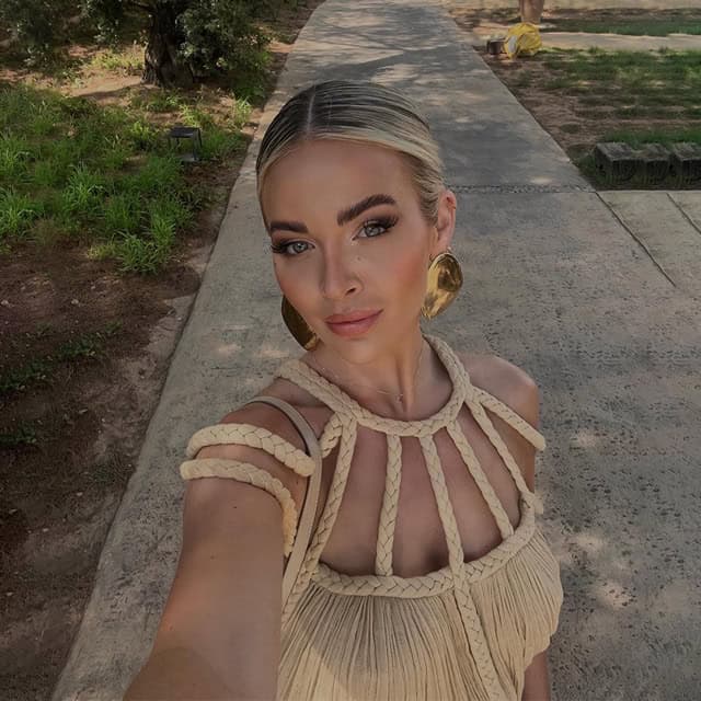 Woman wearing fashionable dress with bold jewelry, walking outdoors on a sunny day.