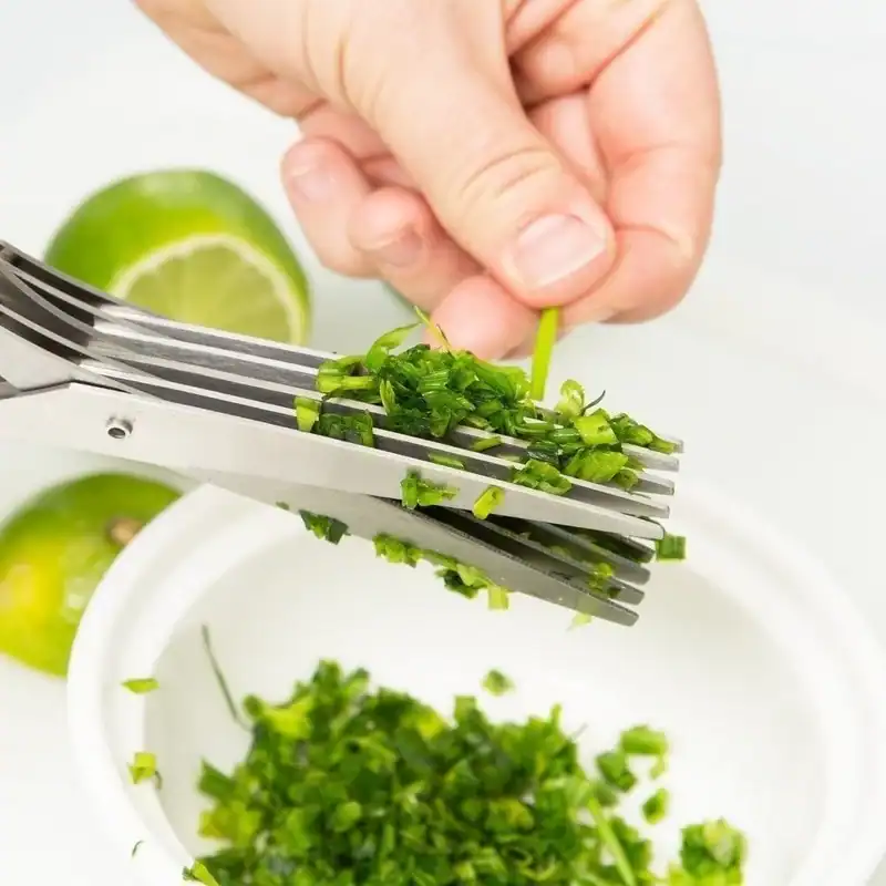 Close-up of a hand finely chopping green chives with a knife over a white bowl, with lime slices in the background, emphasizing fresh ingredients for healthy meals.