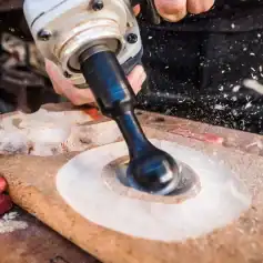A close-up of a power drill making a circular hole in a wooden surface, with wood dust flying around, demonstrating woodworking craftsmanship.
