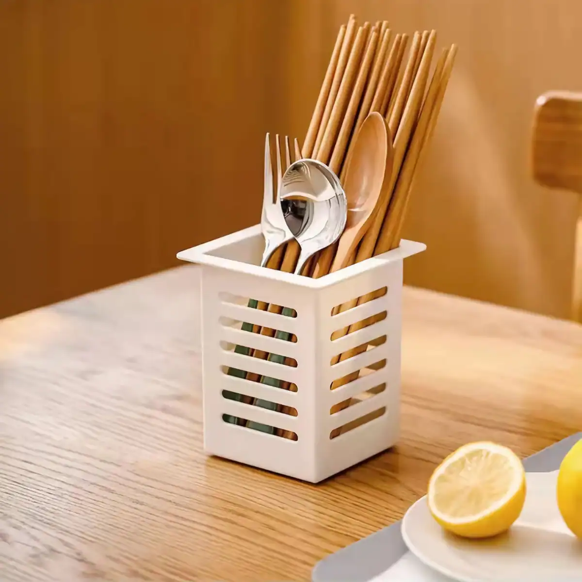 A stylish white plastic cutlery holder on a wooden table, containing wooden chopsticks, a stainless steel fork, and a spoon. Perfect for organizing utensils in restaurants or home kitchens to enhance dining convenience.