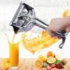 Bright orange juice pouring from a stainless steel juicer into a glass, with fresh oranges, lemons, strawberries, and kiwis on a wooden table, emphasizing healthy lifestyle and fresh ingredient use.