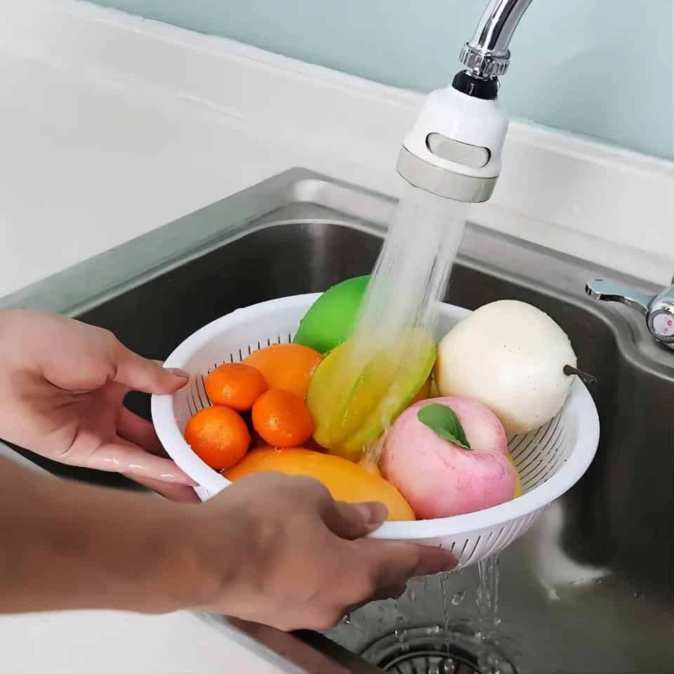 Alt text: Washing fresh fruits in a white bowl under running water at kitchen sink for cleanliness and safety.