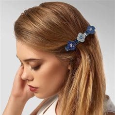 A woman with long, auburn hair wears a decorative floral hair clip adorned with blue and silver stones. The accessory adds a stylish touch to her elegant look.
