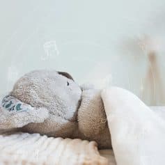 Optical illusion of a plush teddy bear relaxing with a cozy blanket, surrounded by playful musical note and cartoon-themed graphics.