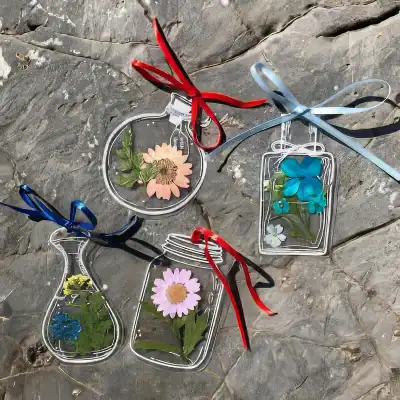 Colorful glass flowers and leaves inside transparent decorative frames with ribbons.