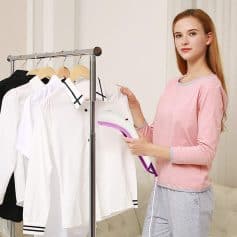 A woman using a portable garment steamer to press white and black shirts, showcasing professional clothing care at Monalisa Store for optimal wardrobe maintenance.