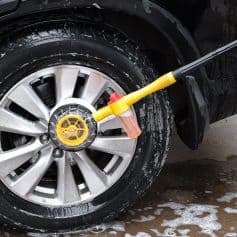 High-pressure car wash sprayer cleaning car tire and wheel for detailing and vehicle care.