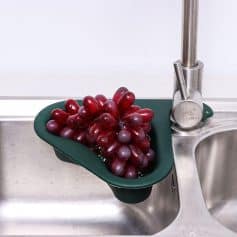 Fresh red grapes placed in a green colander on a stainless steel kitchen sink with modern faucet.