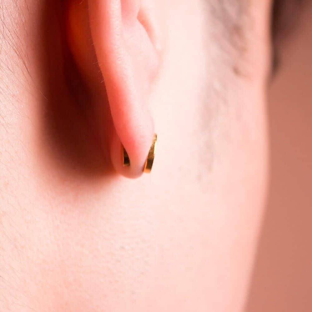 Close-up of a gold hoop earring on a person's earlobe, showcasing elegant jewelry. Perfect for bridal or everyday fashion.