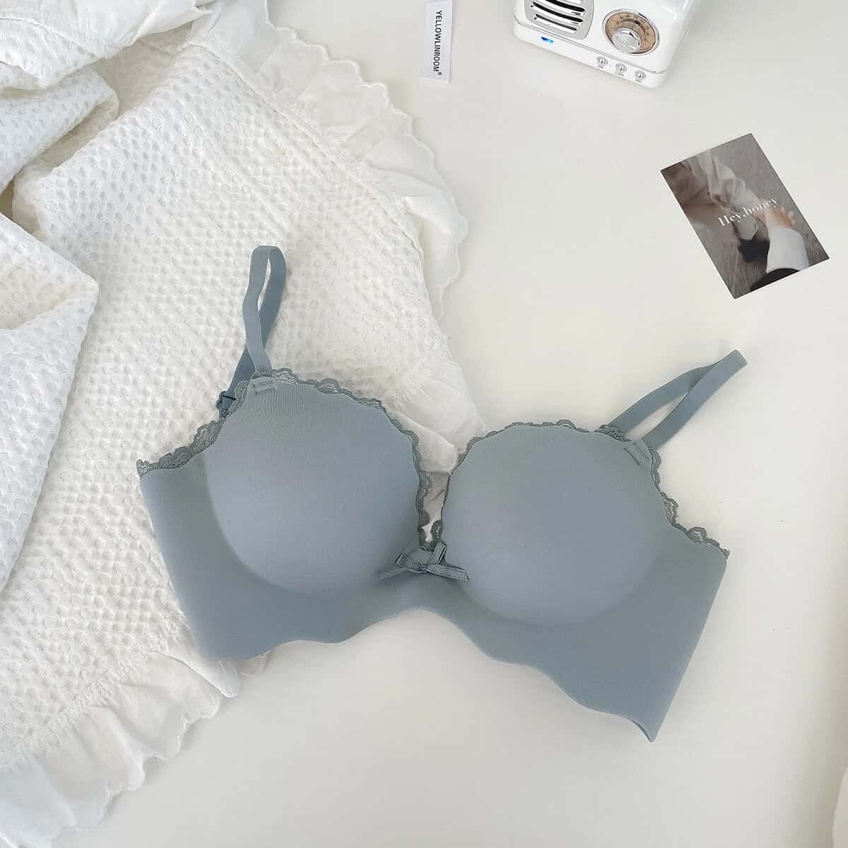 Elegant light gray bra with lace details displayed on a cozy white bed, highlighting premium lingerie and stylish accessories at Monalisa Store.