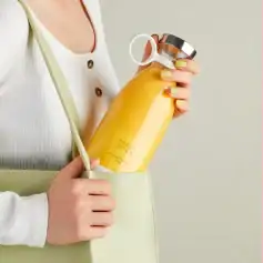 Fresh juice bottle held by a woman with a light green bag, showcasing a healthy lifestyle and beverage options available at Monalisa Store.
