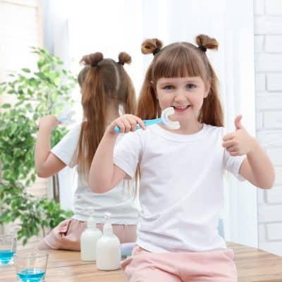 Young girl with a toothbrush showing healthy teeth, bright smile, and playful attitude, emphasizing children's dental health and oral hygiene at Monalisa Medical store.