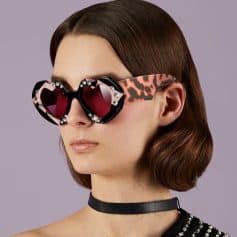 Stylish heart-shaped sunglasses with red lenses, adorned with rhinestones, featuring a leopard print detail on the arms, perfect for high-fashion accessories.