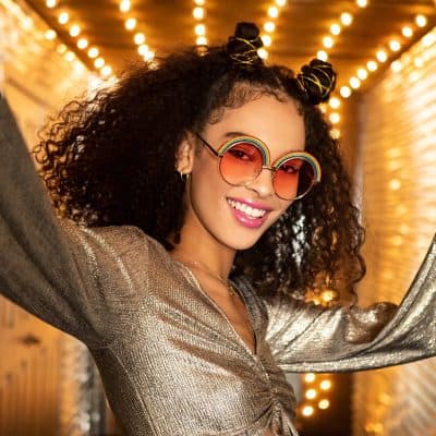 Stylish woman wearing colorful, rainbow-inspired sunglasses and golden attire at Monalisa Store, showcasing fashionable eyewear collection in a vibrant, well-lit setting perfect for trendy eyewear shopping.