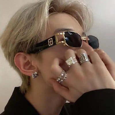 Stylish black sunglasses with gold detailing, paired with multiple luxury rings and diamond earrings for a high-end fashion statement.