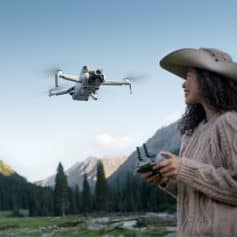 A woman flying a drone outdoors in mountain scenery, taking aerial photos with remote control, showcasing advanced camera drone technology for scenic photography and videography.