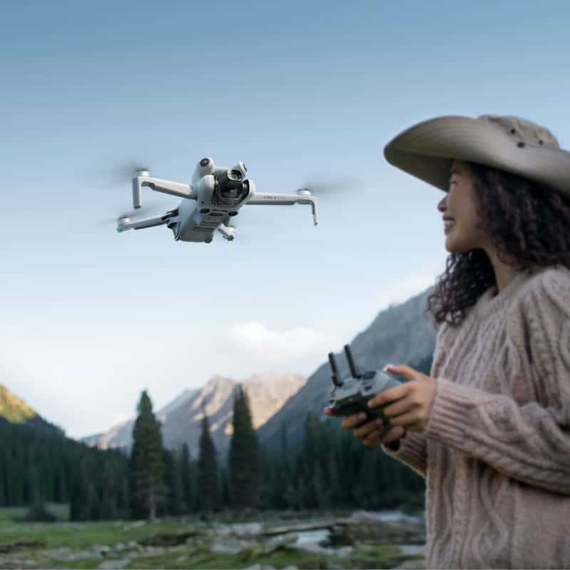 A woman flying a drone outdoors in mountain scenery, taking aerial photos with remote control, showcasing advanced camera drone technology for scenic photography and videography.