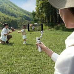 Capturing kids playing with football in a lush green park, scenic mountains in the background, and a person filming with a modern gimbal.