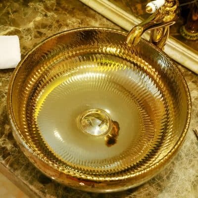 Gold bathroom sink with intricate textured details, decorative faucet, and marble countertop, enhancing upscale and stylish bathroom interiors.